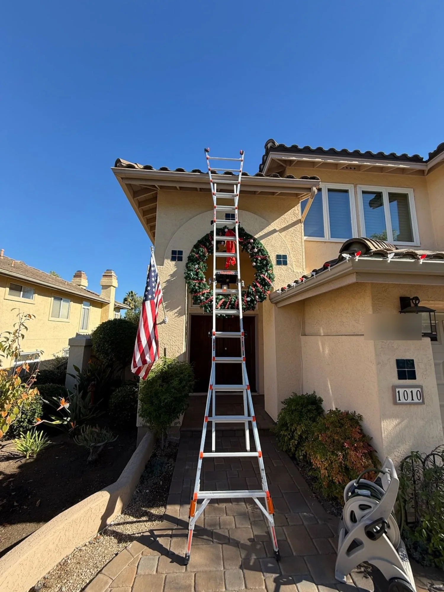 Illuminate crew installing a giant Christmas wreath above an Escondido front entry
